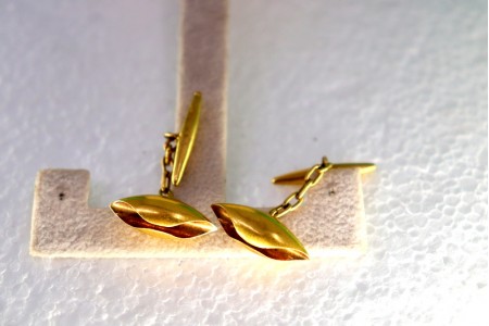 Botões de punho em ouro em formato de folha fechada.